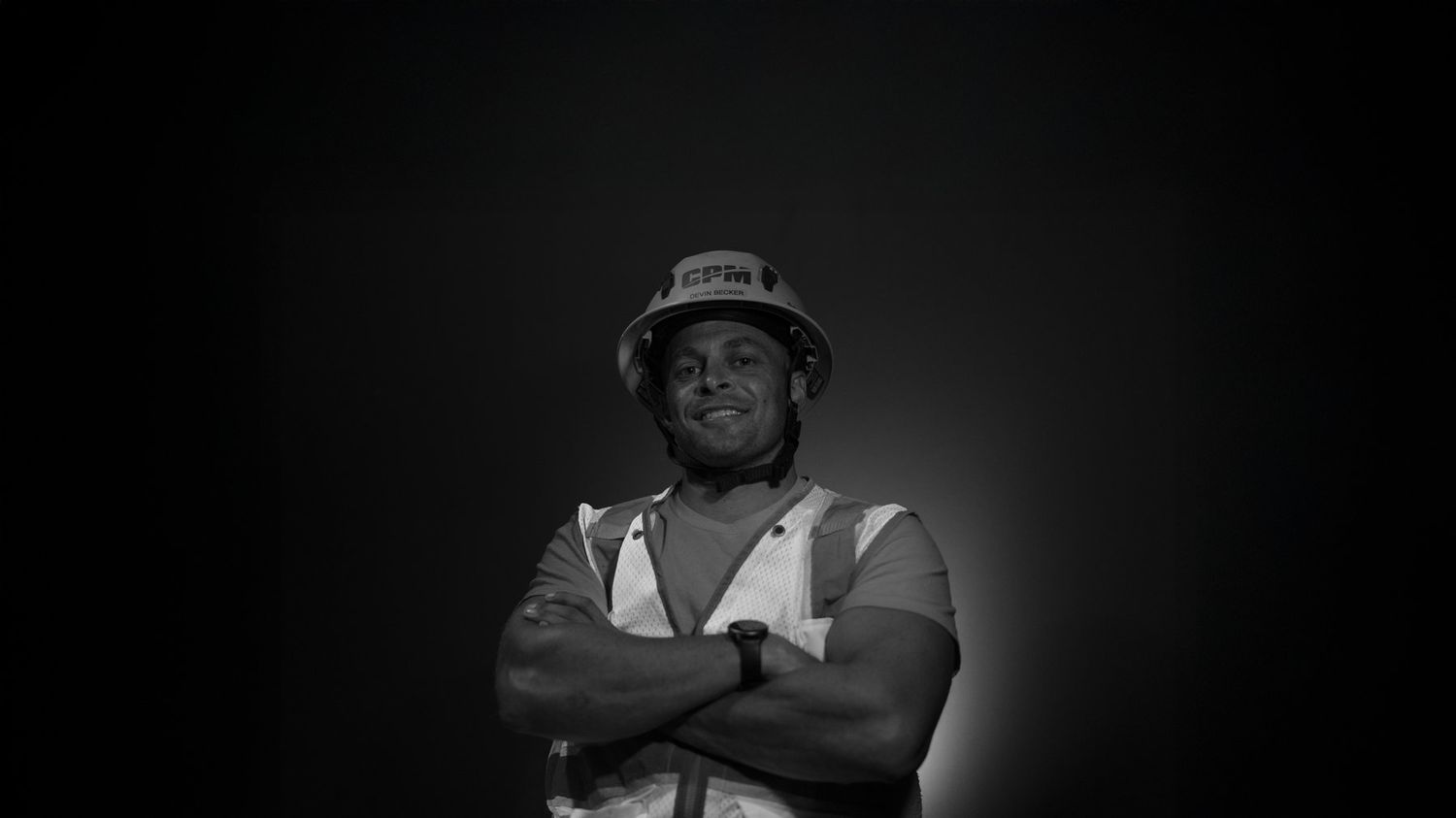 Devin Becker in a CPM hard hat, arms crossed, black and white portrait