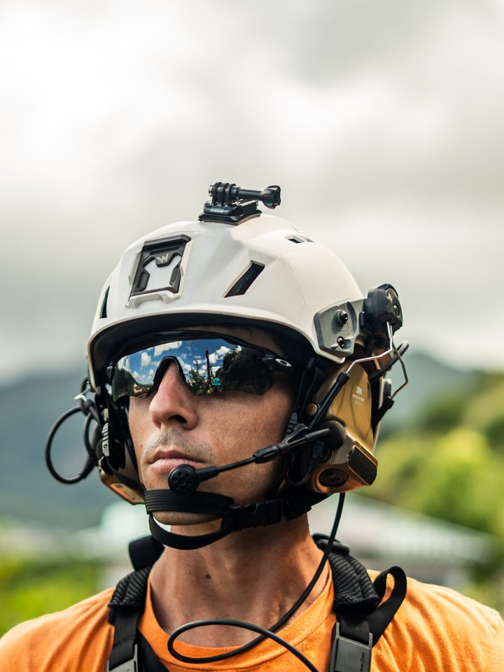 Rope-access technician in a white helmet and sunglasses with Hawaii mountains behind him