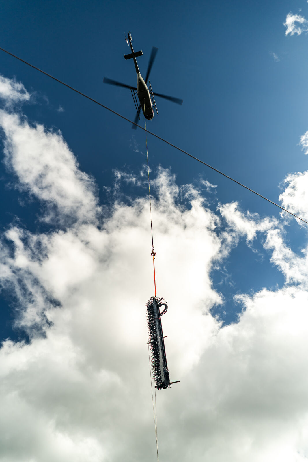 Helicopter flying a barrier post overhead against a blue sky